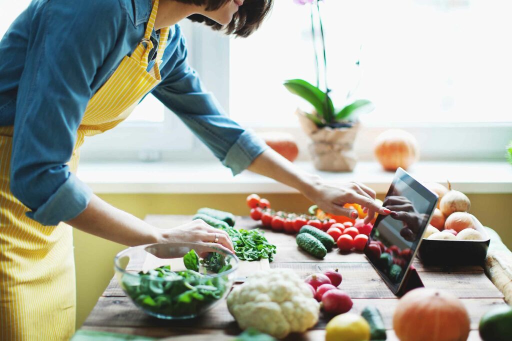 Woman preparing fresh vegetables while referencing recipes from a tablet device