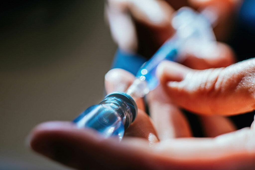 Hands extracting COVID-19 vaccine from bottle using syringe