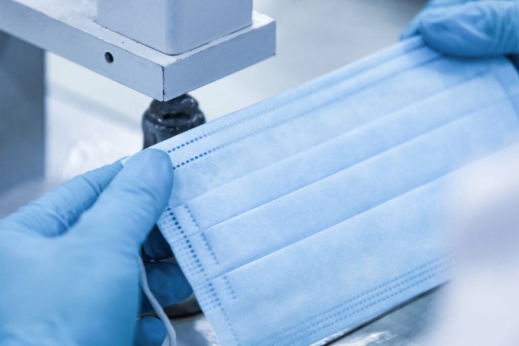 Hands inspecting a surgical mask during manufacturing